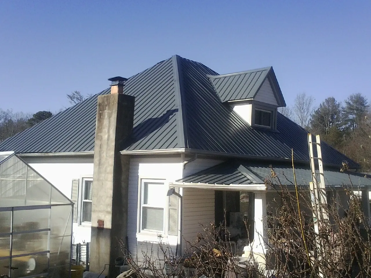 Dark blue standing seam metal roof on a white farmhouse with dormer — Slate & Tile Roof Repair by Roofing Brothers in Belleview