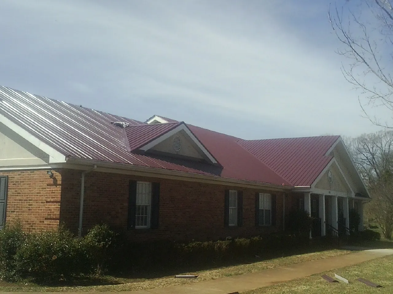 Red metal roof with gabled entries on a long brick building, from a Hail Damage Roof Repair job in Belleview