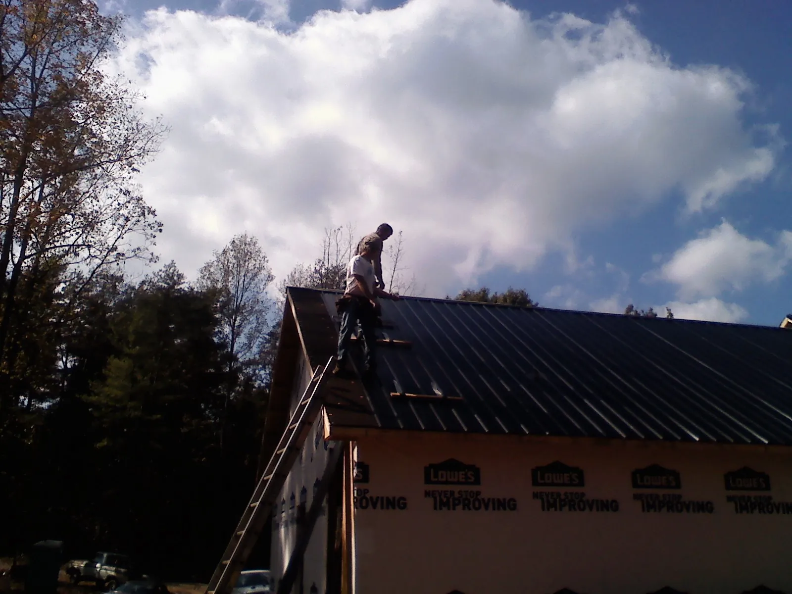 Roofer fastening dark metal panels high against a cloudy sky, from a Roof Inspection job in Belleview